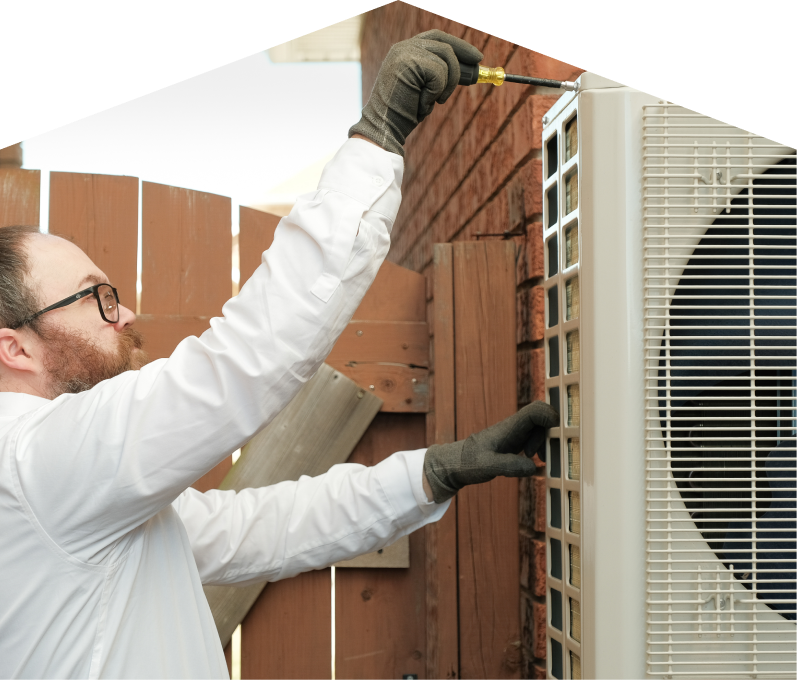 Furnasman service personnel working on an AC condenser, using a screwdriver to secure the unit’s panel outdoors beside a wooden fence. Furnasman service personnel working on an AC condenser, using a screwdriver to secure the unit's panel outdoors beside a wooden fence.