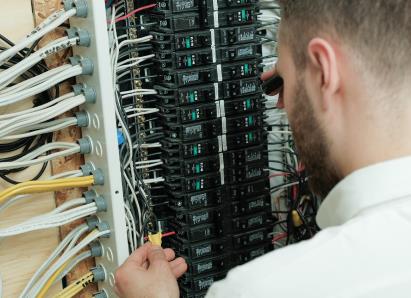 Furnasman electrical technician examining wiring connections inside a circuit breaker panel for a residential service check. Furnasman electrical technician examining wiring connections inside a circuit breaker panel for a residential service check.
