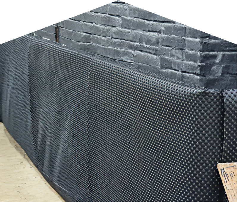 Exterior basement waterproofing completed by Furnasman, showing a sealed foundation wall with dimpled waterproof membrane partially installed on a brick surface, preventing moisture infiltration. Exterior basement waterproofing completed by Furnasman, showing a sealed foundation wall with dimpled waterproof membrane partially installed on a brick surface, preventing moisture infiltration.