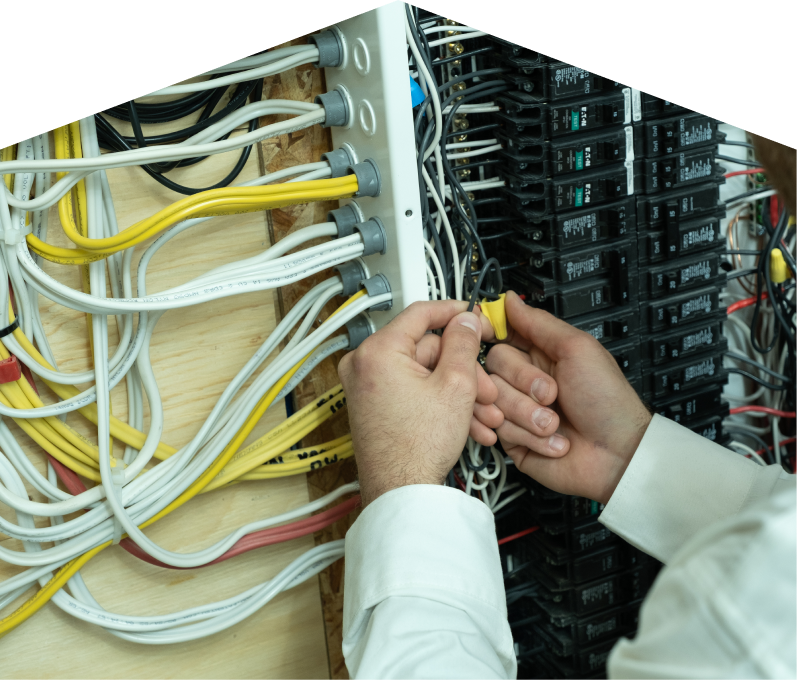 Furnasman service personnel working on electrical installations, connecting wires inside a residential breaker panel with neatly arranged colored cables on a plywood backing. Furnasman service personnel working on electrical installations, connecting wires inside a residential breaker panel with neatly arranged colored cables on a plywood backing.