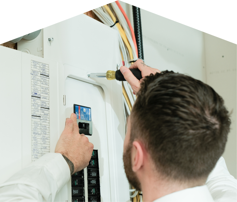 Furnasman electrician using a screwdriver to perform an electrical panel upgrade, working near organized wiring in a residential wall. Furnasman electrician using a screwdriver to perform an electrical panel upgrade, working near organized wiring in a residential wall.