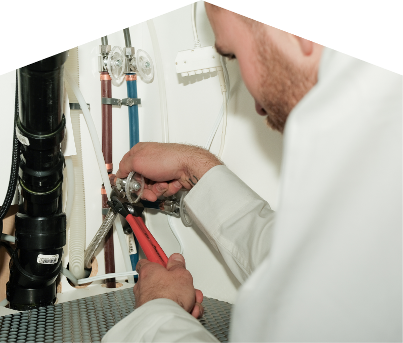 Furnasman plumbing expert tightening connections under a sink during a faucet installation, surrounded by hot and cold water supply lines and PVC drainage. Furnasman plumbing expert tightening connections under a sink during a faucet installation, surrounded by hot and cold water supply lines and PVC drainage.