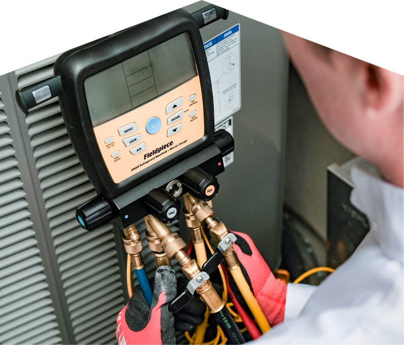 A Furnasman home service crew member uses a digital manifold gauge to check refrigerant levels on an HVAC unit for service. A Furnasman home service crew member uses a digital manifold gauge to check refrigerant levels on an HVAC unit for service.