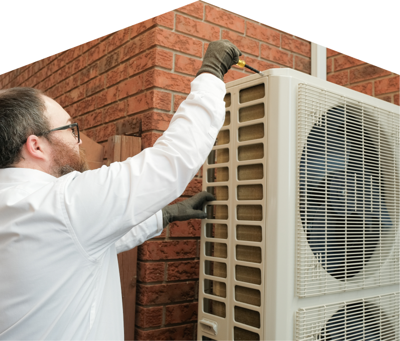 Furnasman HVAC specialist using a screwdriver to complete a heat pump installation beside a brick wall. Furnasman HVAC specialist using a screwdriver to complete a heat pump installation beside a brick wall.