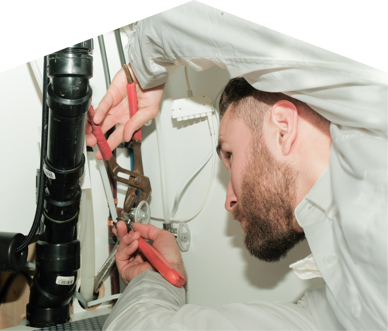 Furnasman plumbing specialist uses hand tools to tighten pipe fittings beneath a sink during a repair, with visible wiring and drainage lines in the background. Furnasman plumbing specialist uses hand tools to tighten pipe fittings beneath a sink during a repair, with visible wiring and drainage lines in the background.