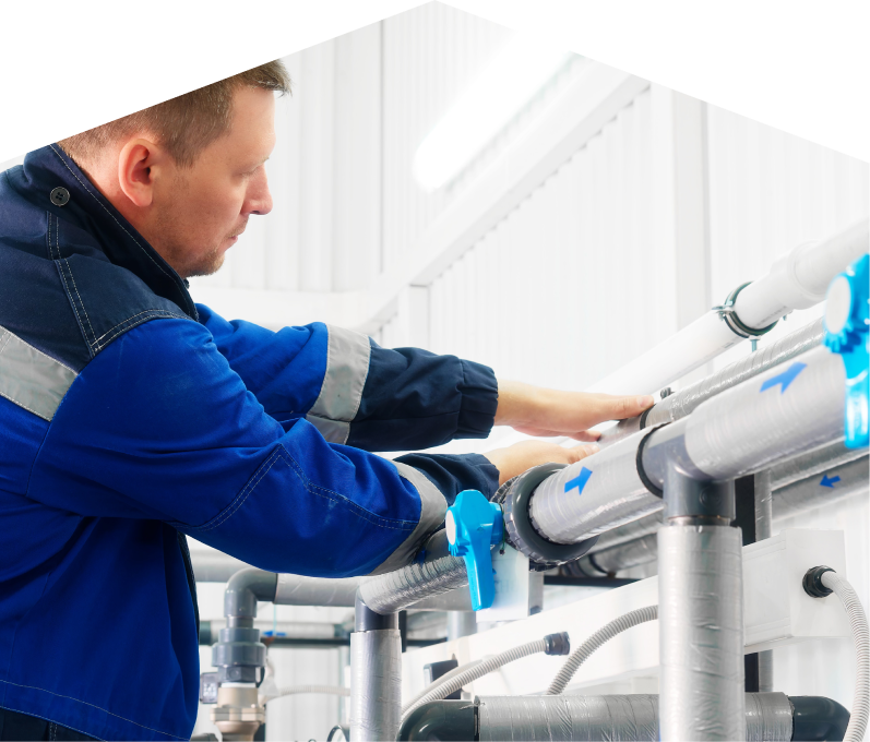Furnasman water damage and restoration specialist in a blue uniform adjusts insulated piping on a water system inside a bright utility room. Furnasman water damage and restoration specialist in a blue uniform adjusts insulated piping on a water system inside a bright utility room.