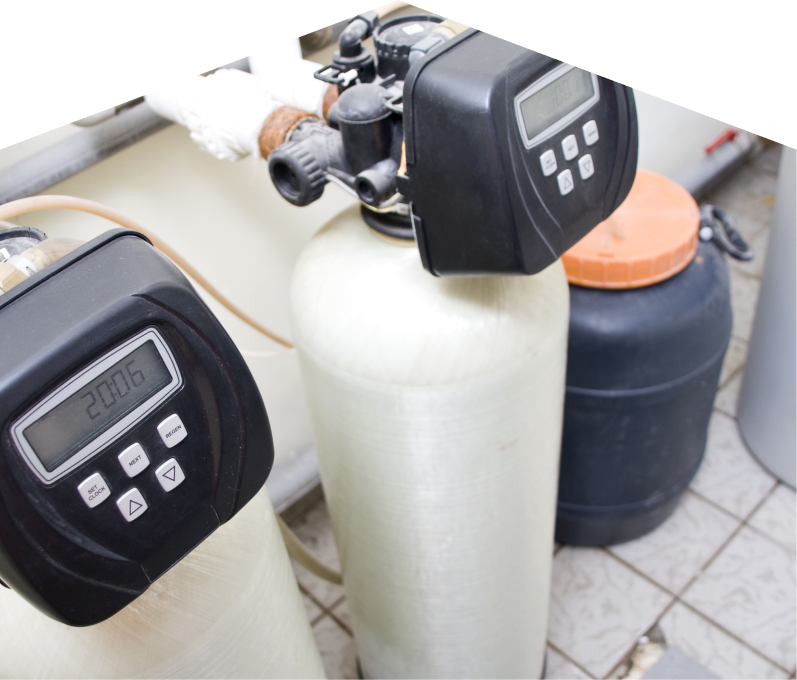 Furnasman water softener installation showing dual resin tanks with digital control heads and a brine tank in a tiled utility area. Furnasman water softener installation showing dual resin tanks with digital control heads and a brine tank in a tiled utility area.