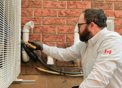 A Furnasman HVAC specialist wearing glasses and gloves uses a diagnostic tool to service an outdoor AC unit beside a brick wall. A Furnasman HVAC specialist wearing glasses and gloves uses a diagnostic tool to service an outdoor AC unit beside a brick wall.