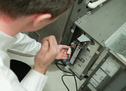 A Furnasman heating technician inspecting internal wiring during a service check on a residential heating unit. A Furnasman heating technician inspecting internal wiring during a service check on a residential heating unit.
