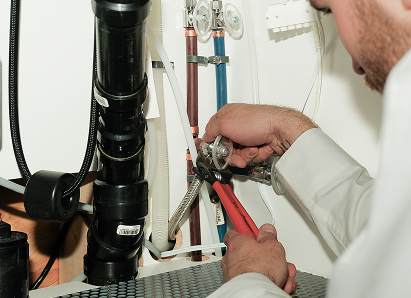 Using two pipe wrenches, a Furnasman professional plumber services a pipe connection near a vertical flue or vent pipe. Using two pipe wrenches, a Furnasman professional plumber services a pipe connection near a vertical flue or vent pipe.